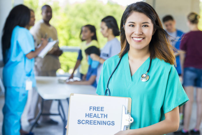 Smiling nurse holding up a "Free Health Screenings" sign
