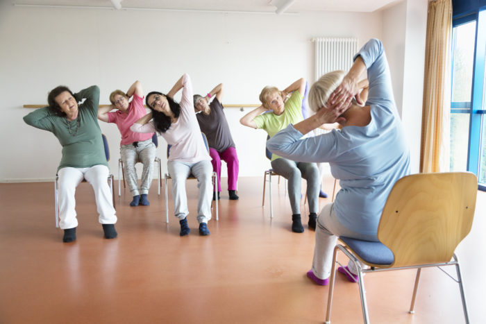 teacher and active senior women yoga class on chairs