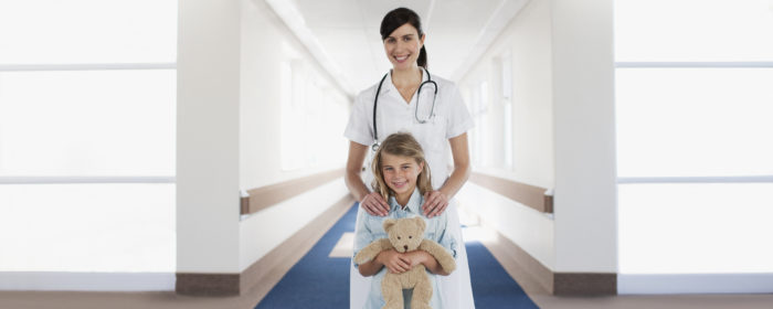 Nurse and child patient with teddy bear in hospital corridor